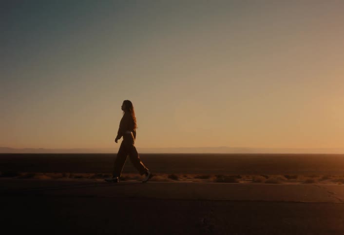 A young woman walks alone on a deserted road, silhouetted against the stunning golden hour sunset