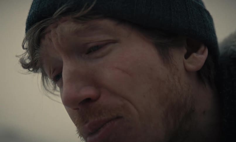A distraught man in winter clothing spits a mouthful of sand in dramatic slow motion