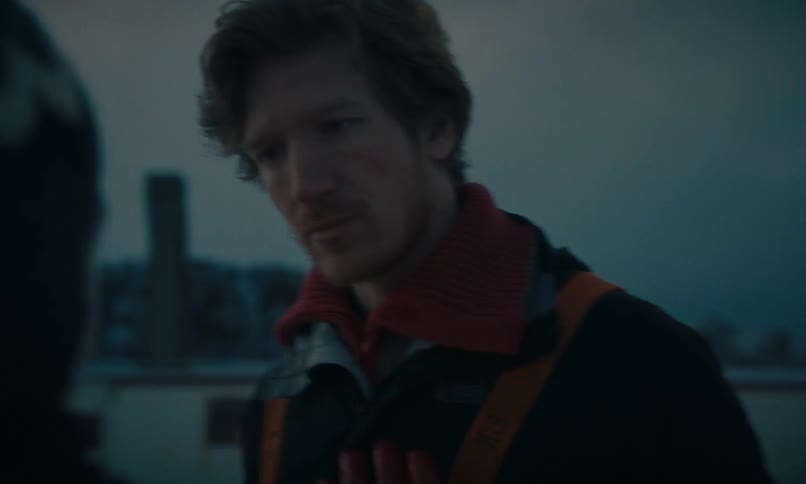 A thoughtful man bundled in a warm winter jacket looks on with concern during an outdoor conversation at dusk