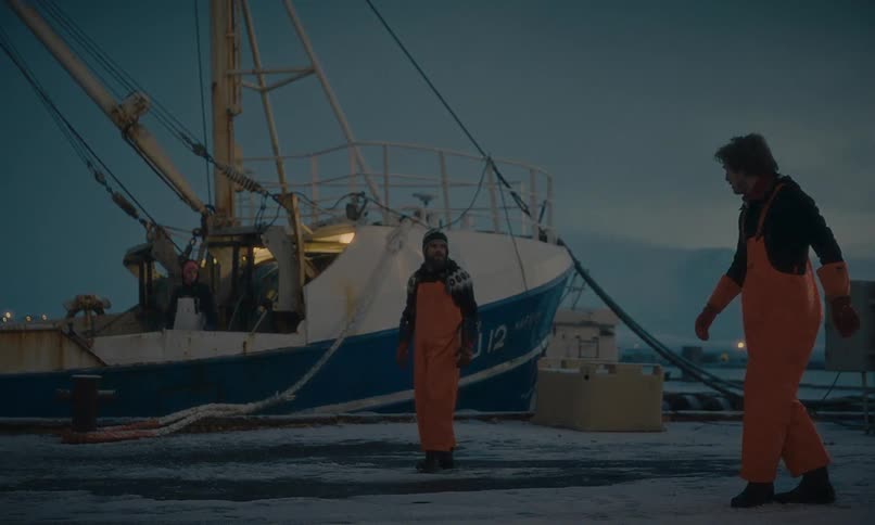 Two fishermen have a somber moment after a fight on a snowy dock, with one helping the other up before they walk away