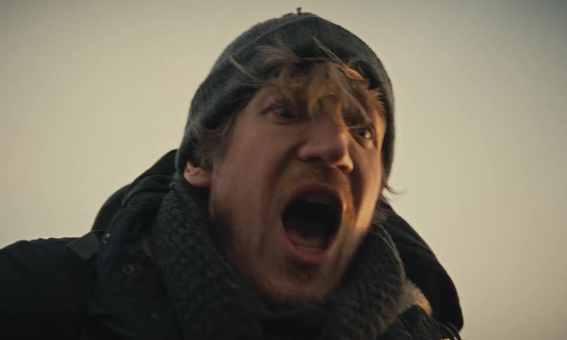 A terrified man wearing a beanie and scarf screams in fear in a dramatic slow motion close-up