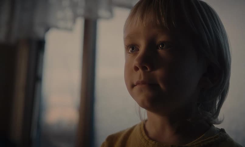 Cinematic close-up of a young boy with blond hair, his face illuminated by gentle window light as he gazes in wonder