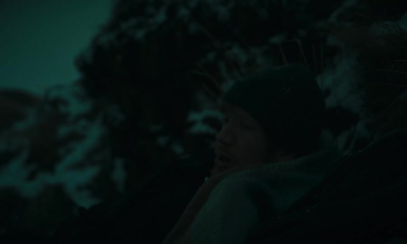 A shivering man wakes up cold and disoriented in a dark, snowy wilderness at night