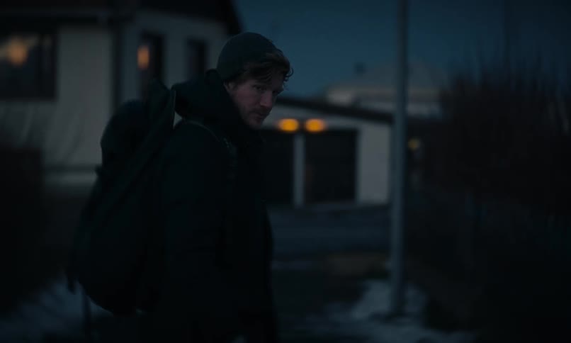 A man with a backpack looks over his shoulder before walking away down a snowy path at dusk in slow motion