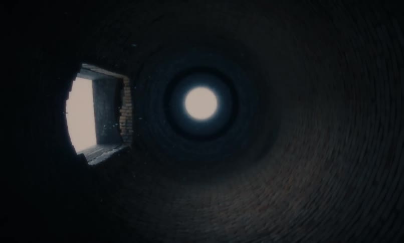 Dust particles drift down a dark, circular brick shaft towards a bright light at the top
