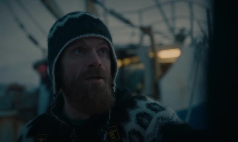Close-up portrait of a rugged bearded fisherman wearing a traditional sweater and winter gear on the deck of a boat at dusk