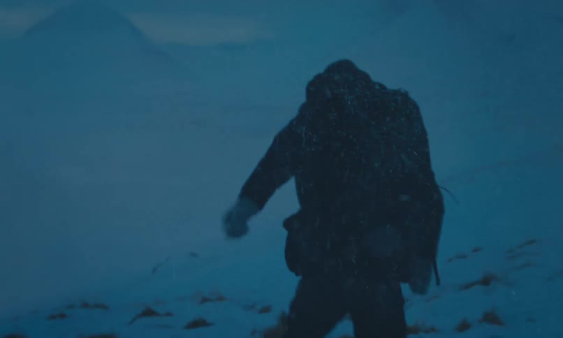 A lone hiker struggles through a fierce blizzard at night, trekking across a desolate snowy mountain landscape in slow motion