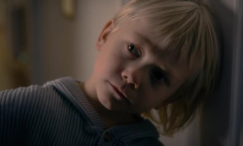 Dramatic close-up of a sad young child with blonde hair leaning against a wall with a somber and thoughtful expression