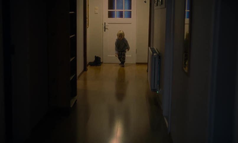 A happy toddler in pajamas energetically crawls, jumps, and runs down a dimly lit hallway at home in slow motion
