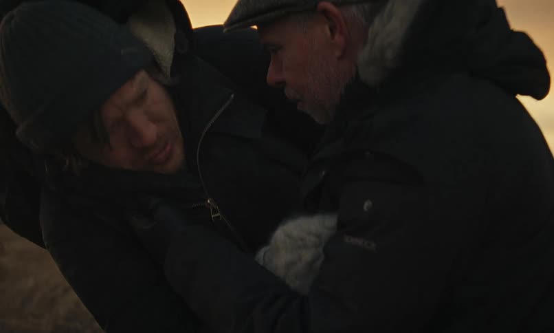 In a dramatic rescue, an older man helps an exhausted hiker to his feet in a cold, desolate landscape