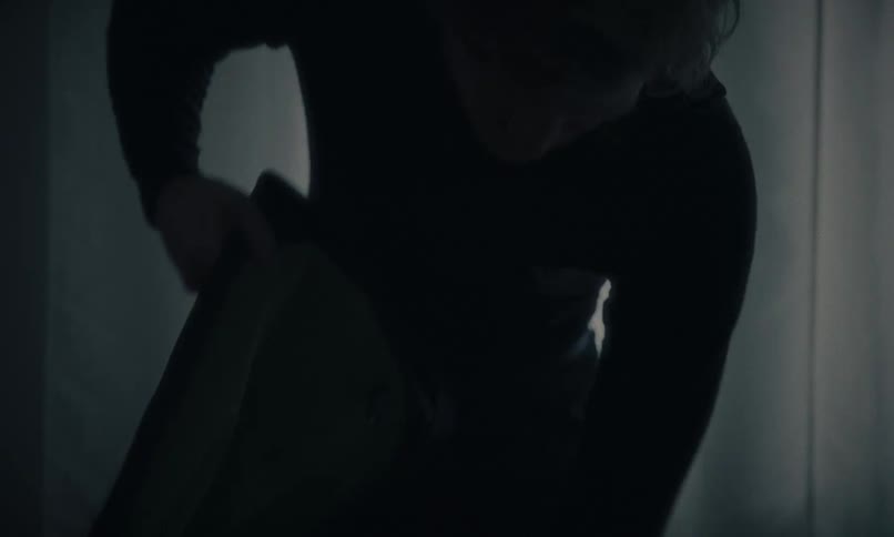 A silhouetted man carefully packs his travel bag in a dark and mysterious room