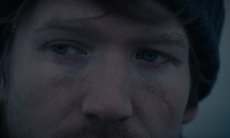 Extreme close-up on the intense, weary blue eyes of a rugged man with a facial scar in the cold, dim light