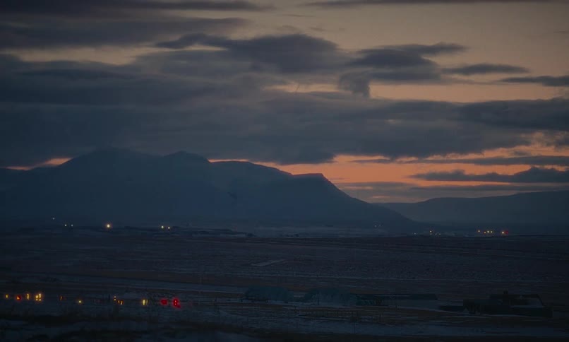 A calm and moody landscape shot of a snowy valley with silhouetted mountains against a cloudy twilight sky