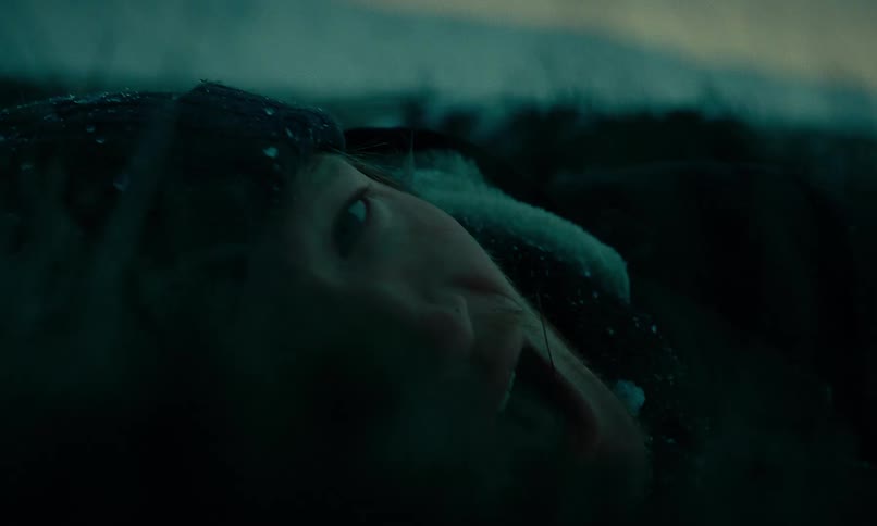 Dramatic close-up of a terrified man's face as he lies on the ground during a dark snowstorm