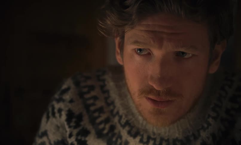 Intense close-up of a contemplative man in a warm sweater staring at something off-screen before drinking from a white mug in a dimly lit room