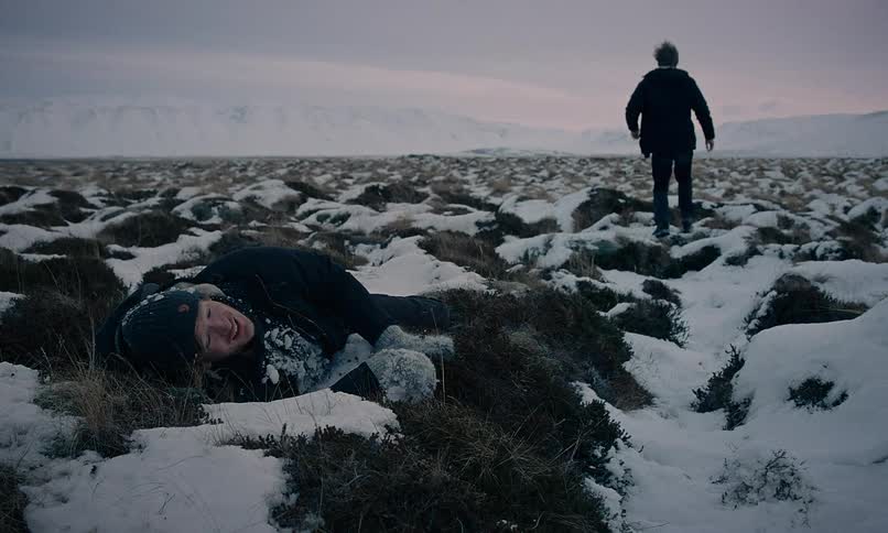 In a bleak, snow-covered landscape, one man walks away leaving his companion lying injured on the frozen ground