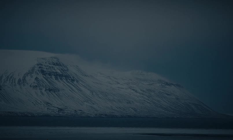 A vast and moody snow-covered mountain range sits under a dark and cloudy sky