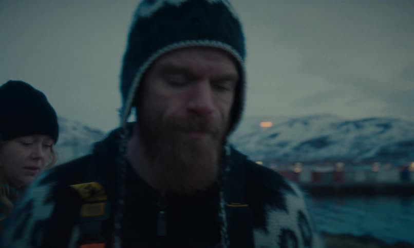 An Icelandic fishing couple walks through a snowy village and has a serious conversation by the harbor at dusk