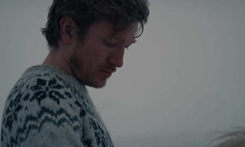 Slow motion close up of a man in a warm sweater affectionately petting a white-maned horse in a gentle snowstorm