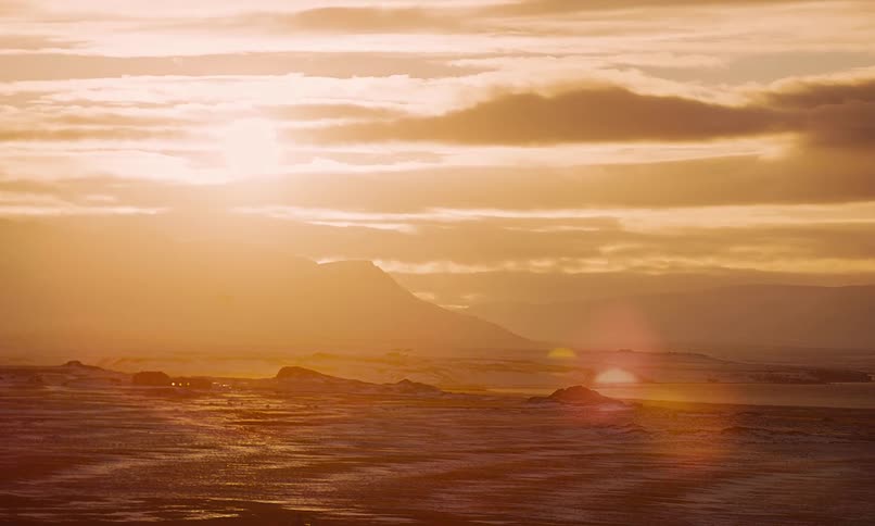 A serene golden sunset casts a warm glow over a vast, snowy Icelandic landscape with mountains in the distance