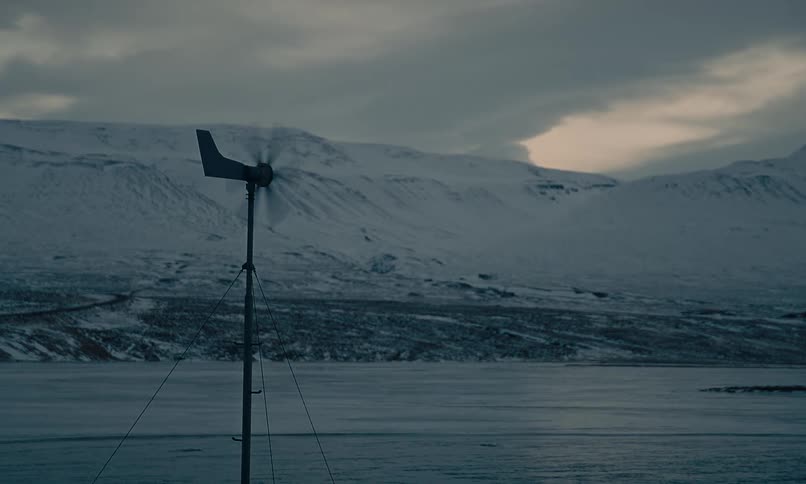 A solitary wind turbine spins in a vast, snow-covered landscape with mountains in the background during a cold winter day