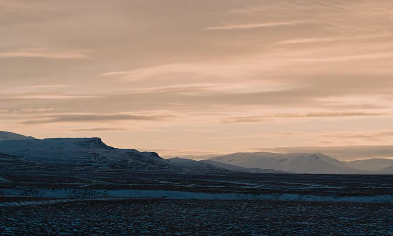 A serene, static view of a vast, rocky Icelandic plain lightly dusted with snow under a soft, golden sunset