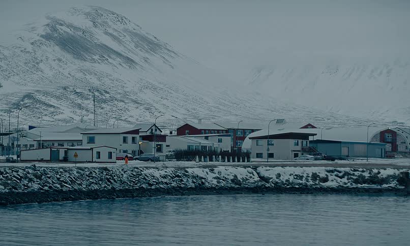 A quiet, snow-covered coastal village rests at the foot of towering mountains on a cold winter day in Iceland