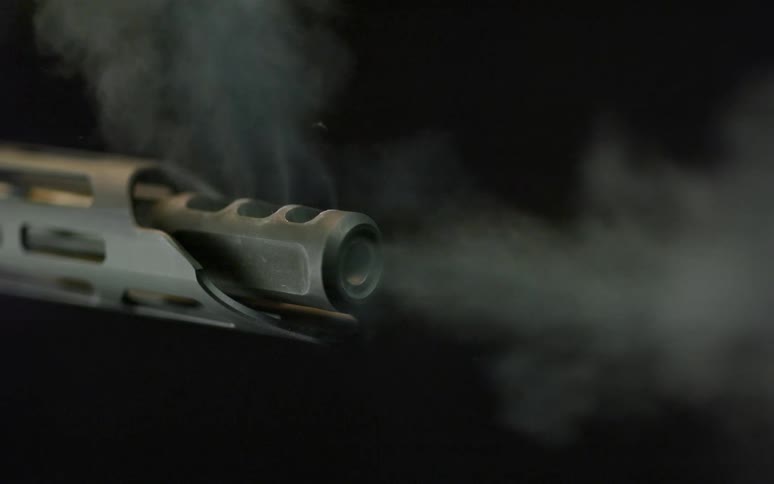 Super slow-motion close-up of a bullet exiting a rifle barrel, surrounded by smoke on a black background
