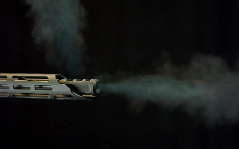 Close-up of a rifle firing a round in super slow motion, showing the bullet and smoke leaving the muzzle against a black background
