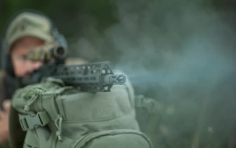 Extreme slow-motion close-up of a rifle barrel firing, showing the muzzle flash and smoke billowing out