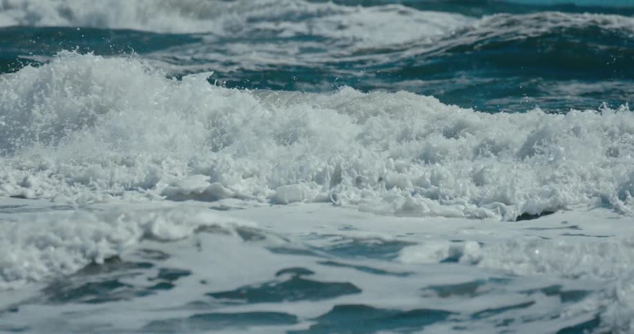 A powerful ocean wave crashes in dramatic slow motion, creating a cascade of white foam