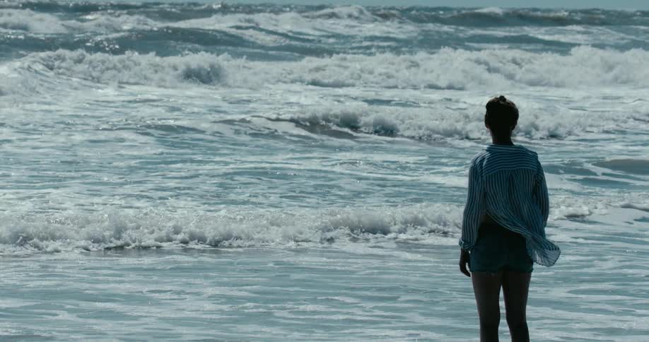 A woman stands still, contemplating the powerful ocean waves crashing on the shore in a mesmerizing cinemagraph