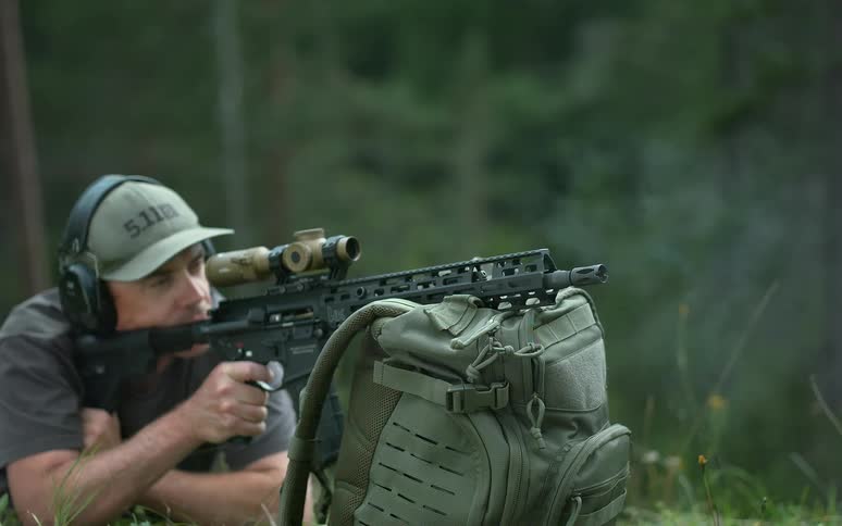 Super slow motion video of a man firing a rifle with a scope while lying prone in the woods
