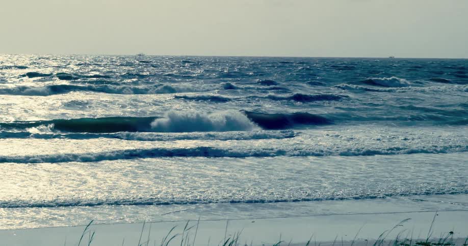 Cinematic slow motion shot of dramatic ocean waves crashing on the shore with sunlight shimmering on the water
