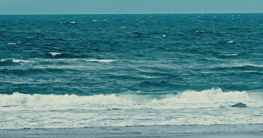 A slow-motion cinematic shot of moody, teal-colored ocean waves breaking on the shore