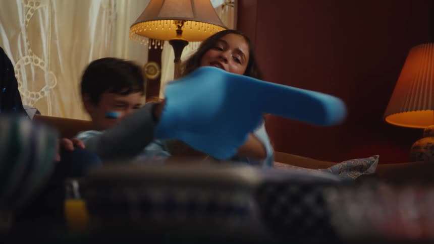 Siblings wearing fan gear get excited and then tense while watching a sports match on the couch with their family