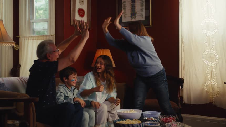 Grandparents and grandchildren erupt in cheers and high-fives while watching a football game at home
