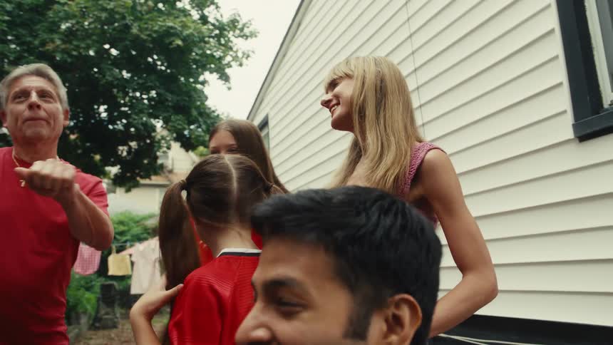 A diverse group of friends and family of all ages laugh, talk, and dance together during a lively backyard party