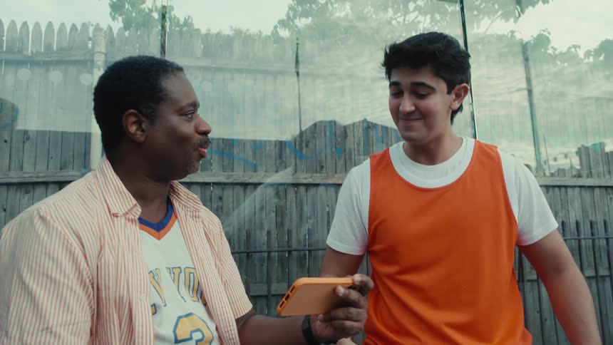 Two diverse friends celebrate excitedly while watching a sports game together on a smartphone outdoors