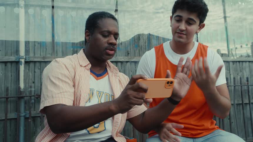An African American coach and a young basketball player have an animated discussion while reviewing a play on a smartphone outdoors