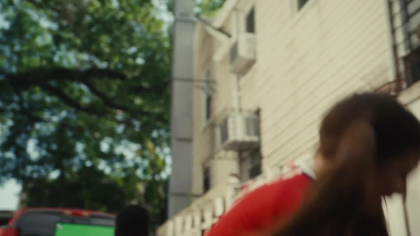 A young girl in a red soccer uniform smiles as she skillfully juggles a soccer ball in slow motion in a residential backyard