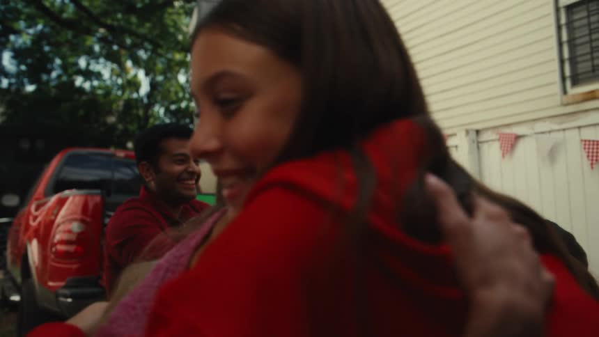 Excited sports fans in red cheer, hug, and high-five in a backyard while watching their team win on a green screen TV