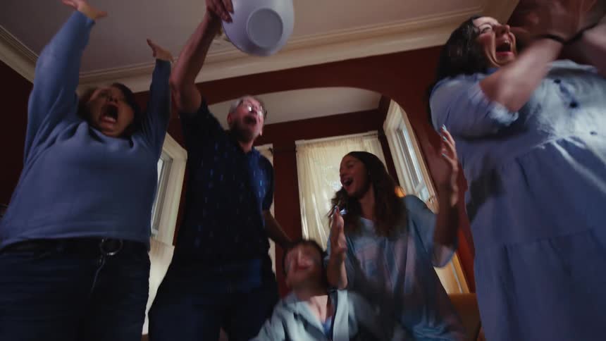 A multi-generational family nervously watches a sporting event at home, then erupts in celebration, throwing popcorn in the air in slow motion