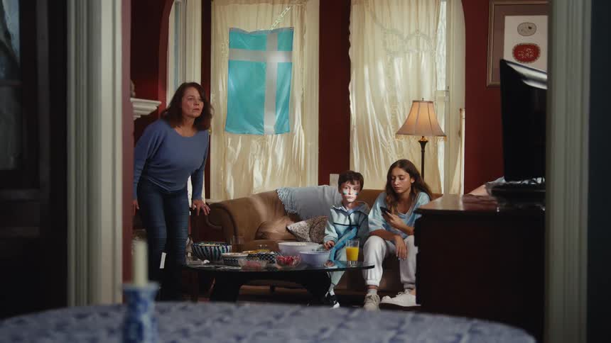 A multi-generational family with grandparents and grandchildren gather together in the living room to watch a football game on television