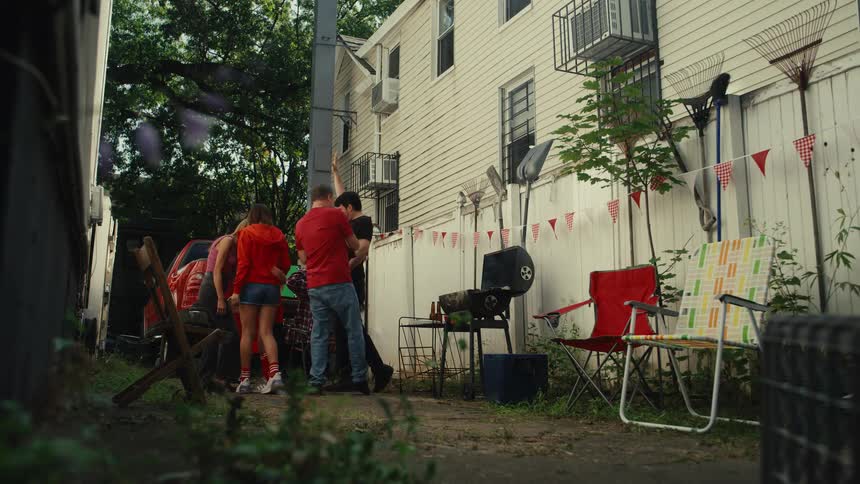 A family and friends wearing matching red team colors cheer and dance with excitement at a backyard tailgate party