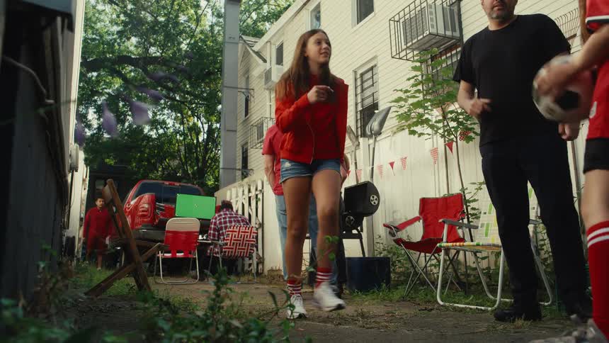 A joyful family in red shirts has fun juggling a soccer ball in slow motion during a backyard tailgate party