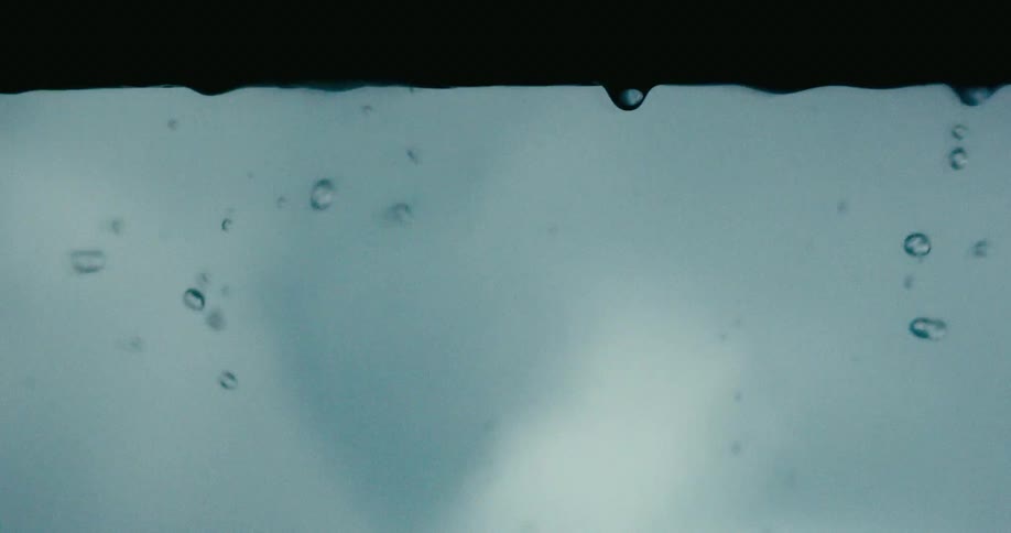 Extreme close-up of mesmerizing water droplets forming and falling in slow motion against a moody background