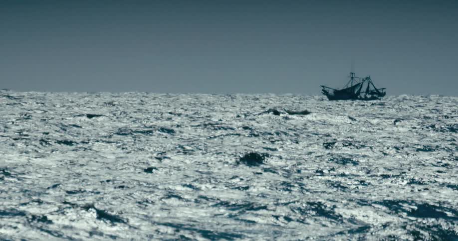 A fishing boat is silhouetted against a grey sky on the vast and choppy open ocean