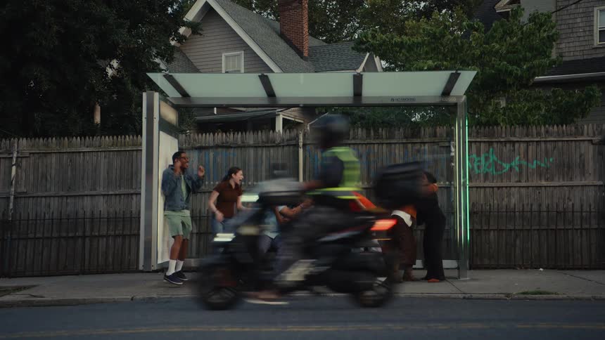 A diverse group of friends erupts in joyful celebration at a suburban bus stop at dusk