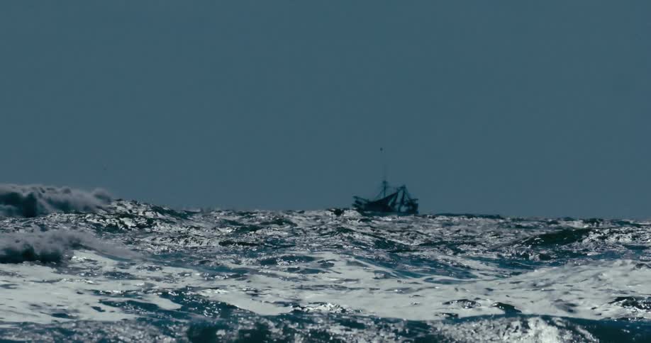 A lone fishing trawler is tossed on the powerful, glistening waves of a turbulent ocean in slow motion
